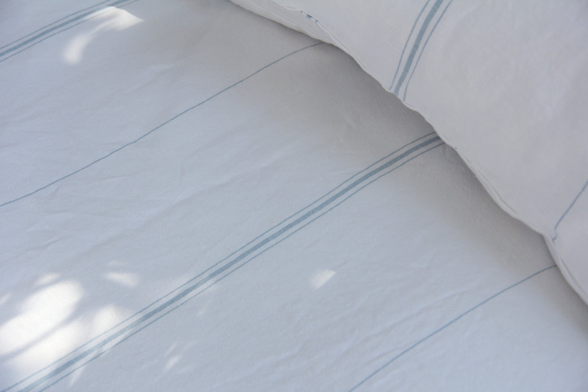 White bed sheets with light blue stripes and soft shadows.