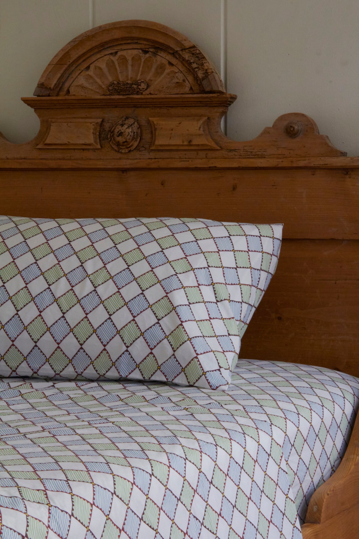 Wooden bed with patterned sheets and pillow in a rustic room.