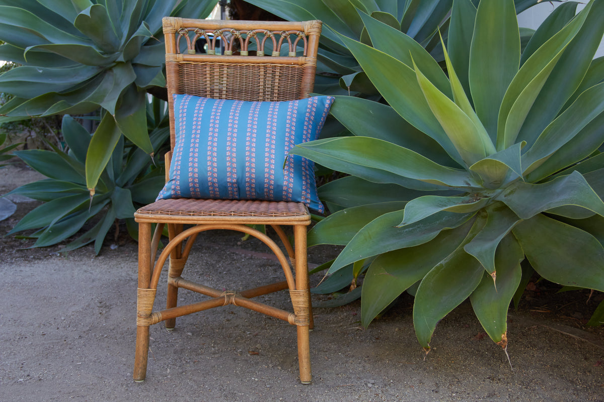 Wicker chair with blue cushion in front of large green plants.
