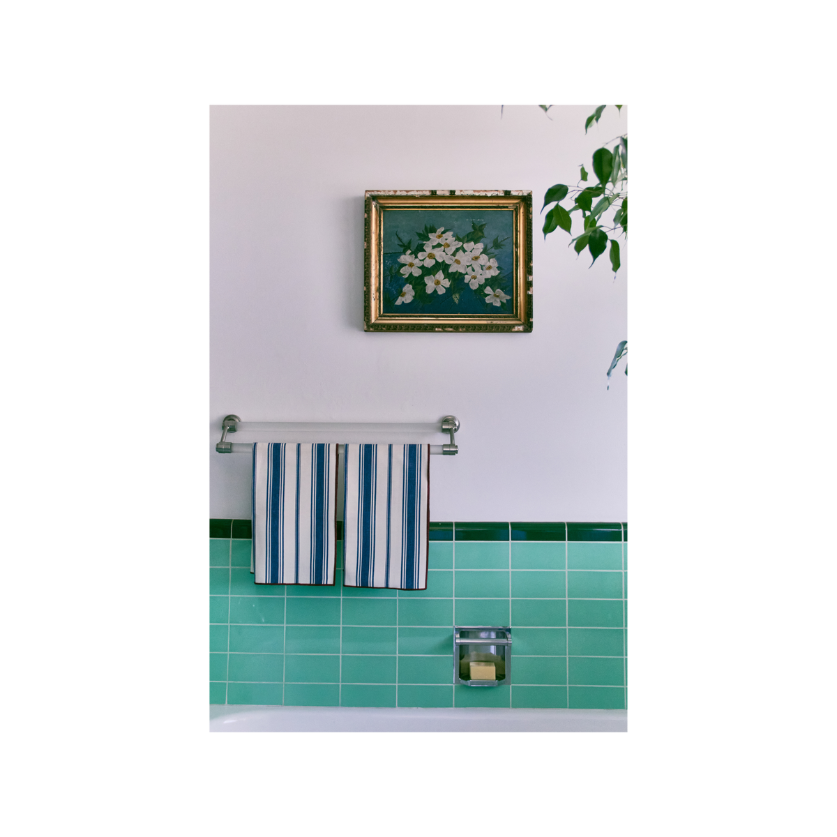 Bathroom with striped towel hanging, green tiles, and a floral painting on the wall.
