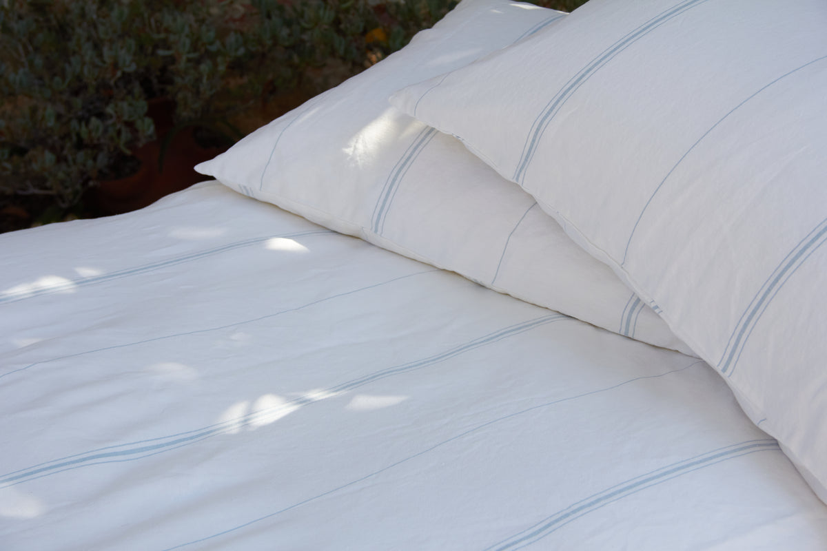 White pillow and sheet with light blue stripes on a bed.