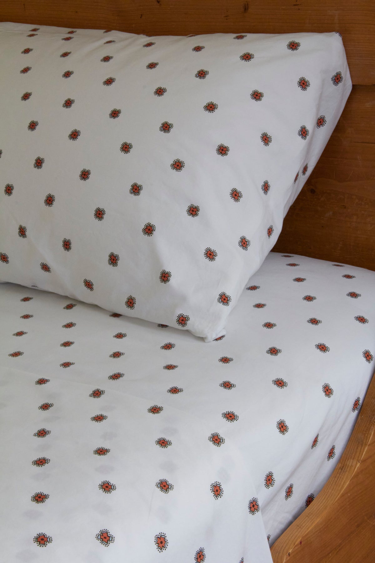 White bed sheets with small red floral patterns on a wooden bed.