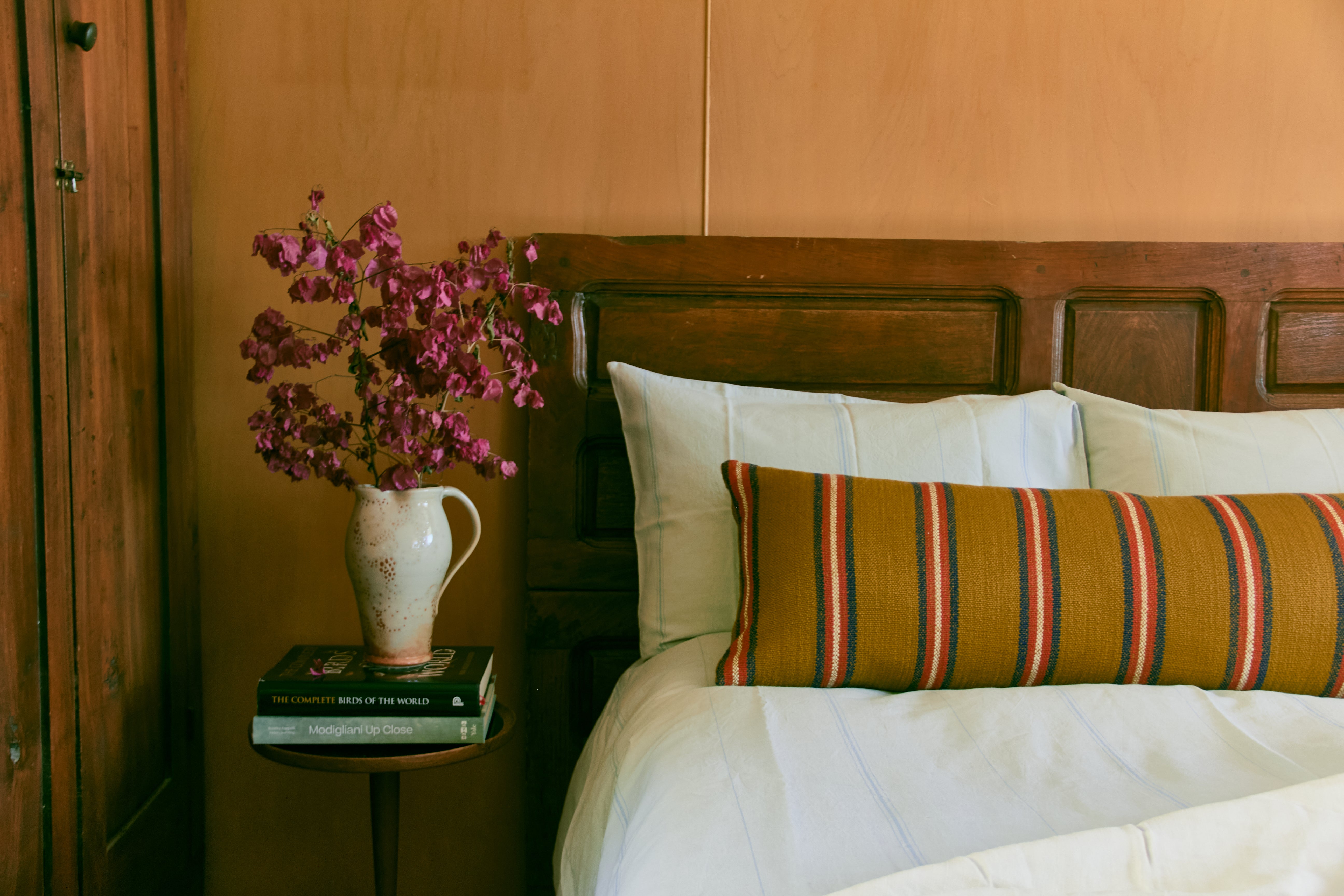 Wooden bed with striped pillow, vase with flowers on side table.