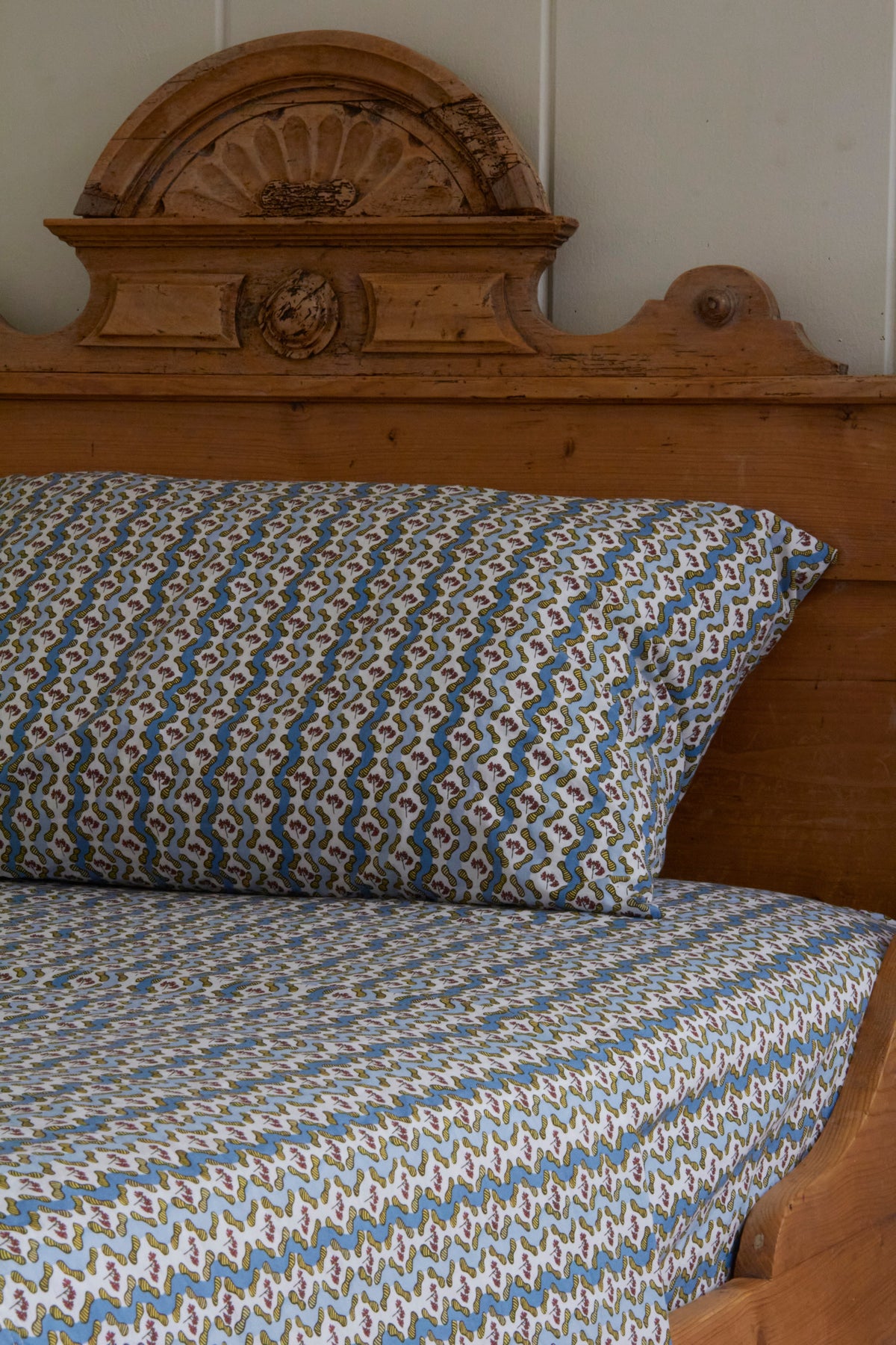 Wooden bed with patterned pillow and sheet in blue and white.